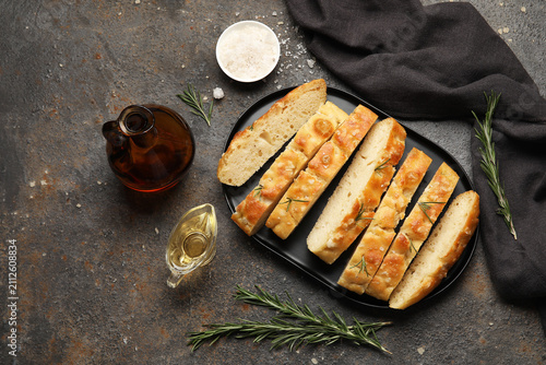 Plate with pieces of traditional Genovese focaccia and ingredients on black grunge background