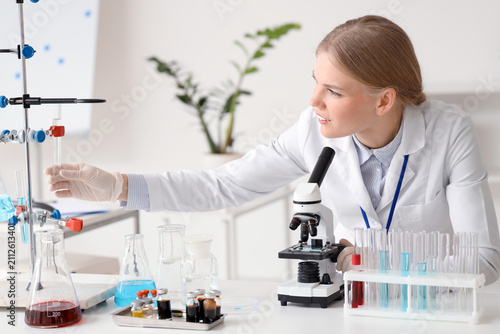 Female scientist with test tube and microscope working at table in laboratory