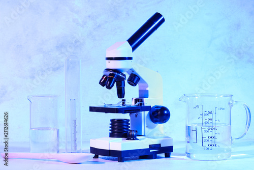 Modern microscope, spoon and laboratory glassware with liquid on blue background