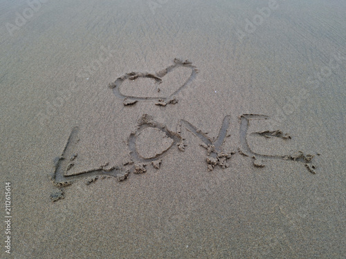 word love and heart drawn in the wet sand on a beach
