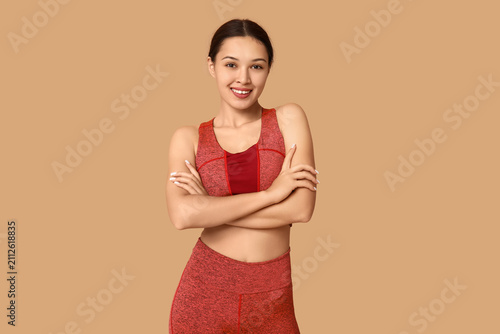 Portrait of young woman in sportswear on beige background