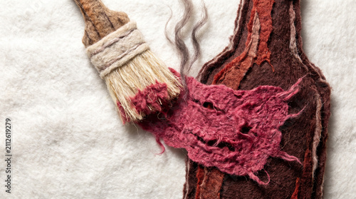 Textile art depicting paintbrush applying color to a wine bottle  