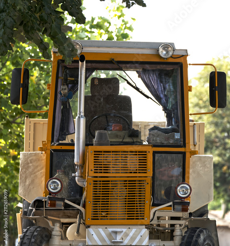Old Yellow tractor stands parked beneath green trees