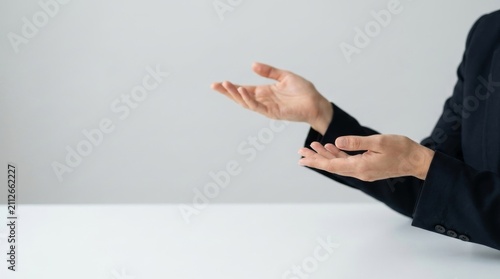 Professional Business Person in Dark Suit Making Open Hand Gestures of Welcome and Explanation Over a Clean White Desk with Copy Space