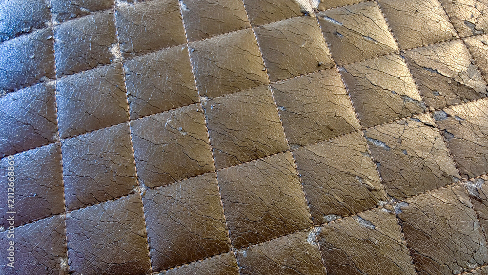 Obraz premium Worn quilted brown synthetic leather upholstery with cracked texture and peeling surface showing damage from wear, a deteriorating fabric background