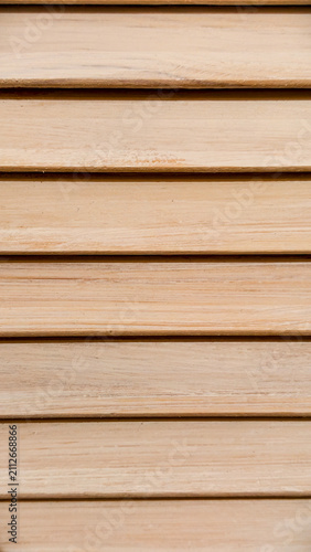 Close up view of natural wood louver patterns, forming a textured background with horizontally arranged light brown wooden slats and visible grain