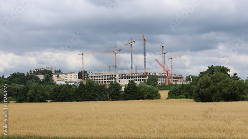 Cuadro en lienzo Large construction site with multiple tower cranes rises beyond a golden grain field beneath dramatic storm clouds