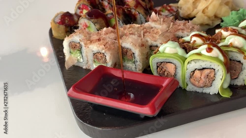 A sushi chef carefully pours fresh soy sauce into a small dipping dish beside an elegant assortment of rolls. Final serving touches before the meal begins.