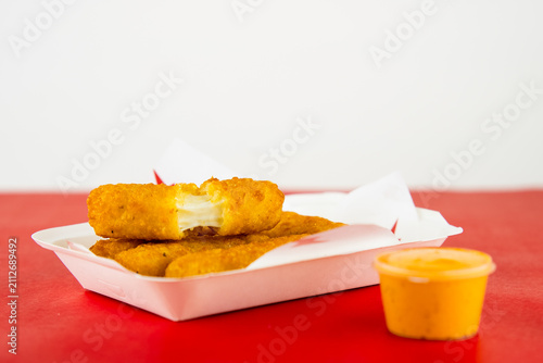 Картината върху платно Golden crispy mozzarella sticks with melted cheese and dipping sauce on red surf