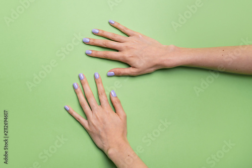 Caucasian woman hands with lavender nail polish on green