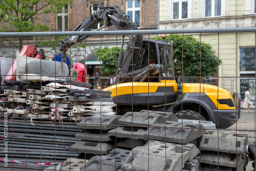 Фотография A construction site behind a metal mesh fence, a yellow and black excavator