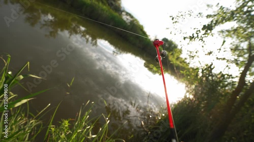 Fishing rod bending and vibrating with bell indicator reacting to fish strike on river. Concept of freshwater fishing and outdoor recreation