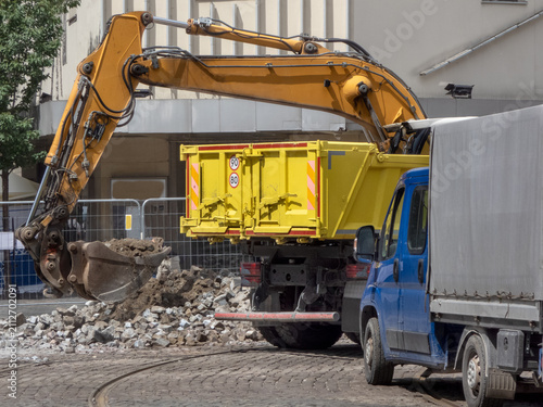A yellow hydraulic excavator next to a large, yellow RORO (Roll-On/Roll-Off) skip container. commercial waste removal services. A blue truck  for hauling away the debris. Demolition operations. 