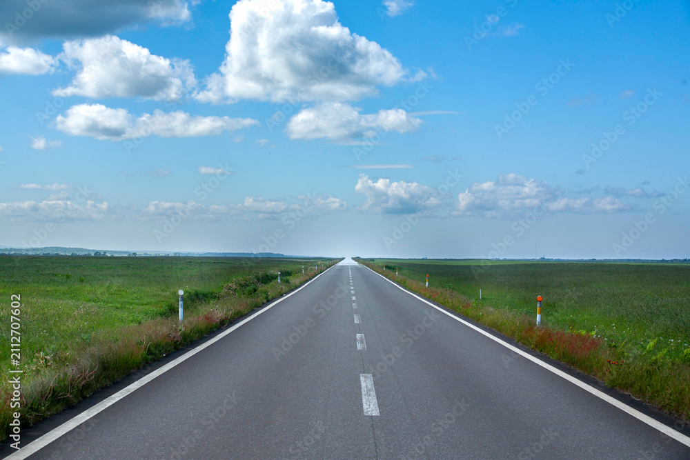 Obraz premium Straight highway stretching across vast Hokkaido grassland under blue sky and white clouds