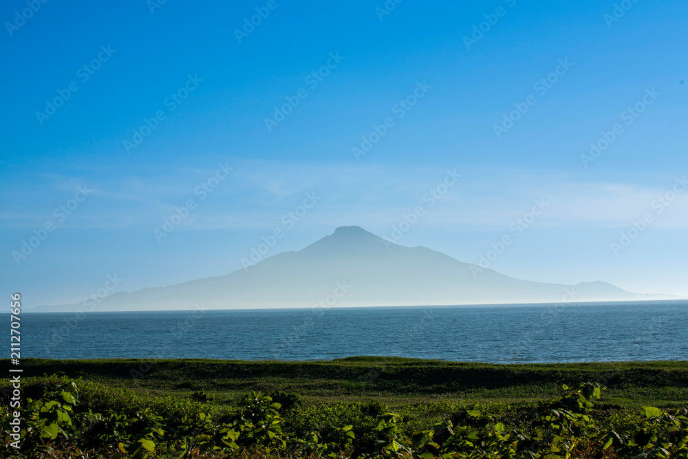 Fototapeta premium Majestic view of Rishiri Island rising from blue sea, seen from Hokkaido coast
