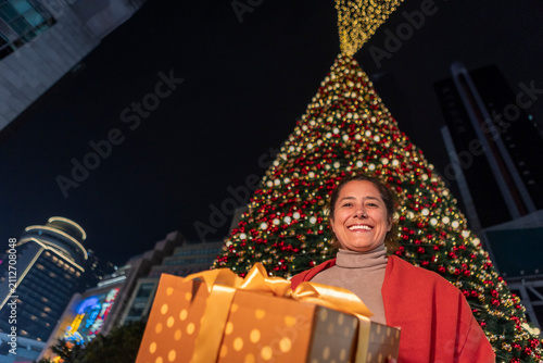 Smiling woman with gift box by giant Christmas tree