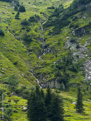 Scenic Cascading Waterfall on a Mountain Slope in Karpacz, Poland Surrounded by Green Hills and Rocky Landscape in Summer