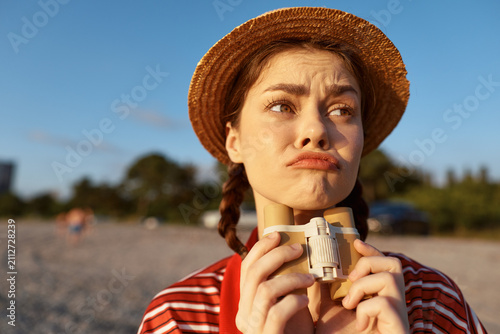 Canvas Print A woman on a beach wears a straw hat and striped shirt, puzzled, holding binoculars, expression curious, seaside mood, summer scene
