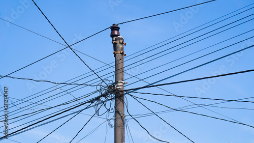 Bild auf Leinwand Utility pole with multiple overhead power lines under a bright blue sky, representing electricity distribution, communication networks, and urban infrastructure