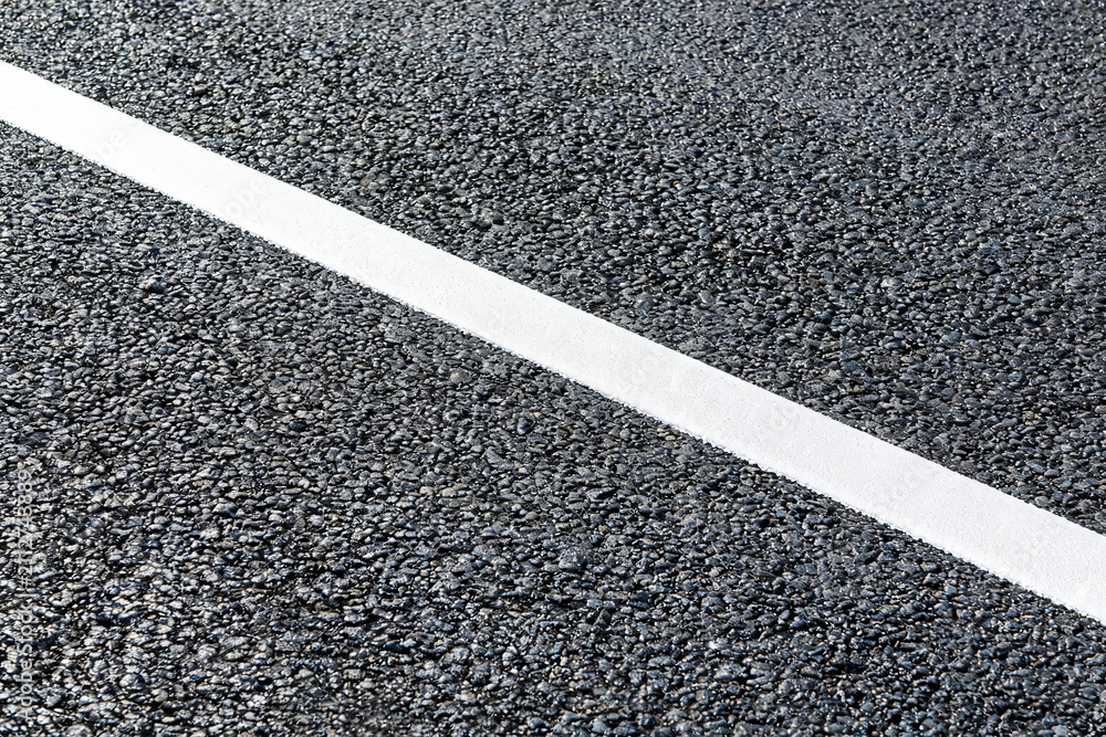 Fototapeta premium A close-up view of a solid white traffic marking line on a rough, dark asphalt pavement surface.