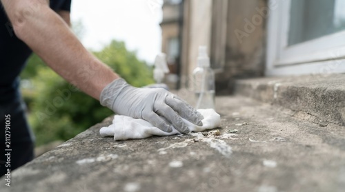 Person wearing gloves cleaning bird droppings from a stone windowsill with disinfectant and cloth