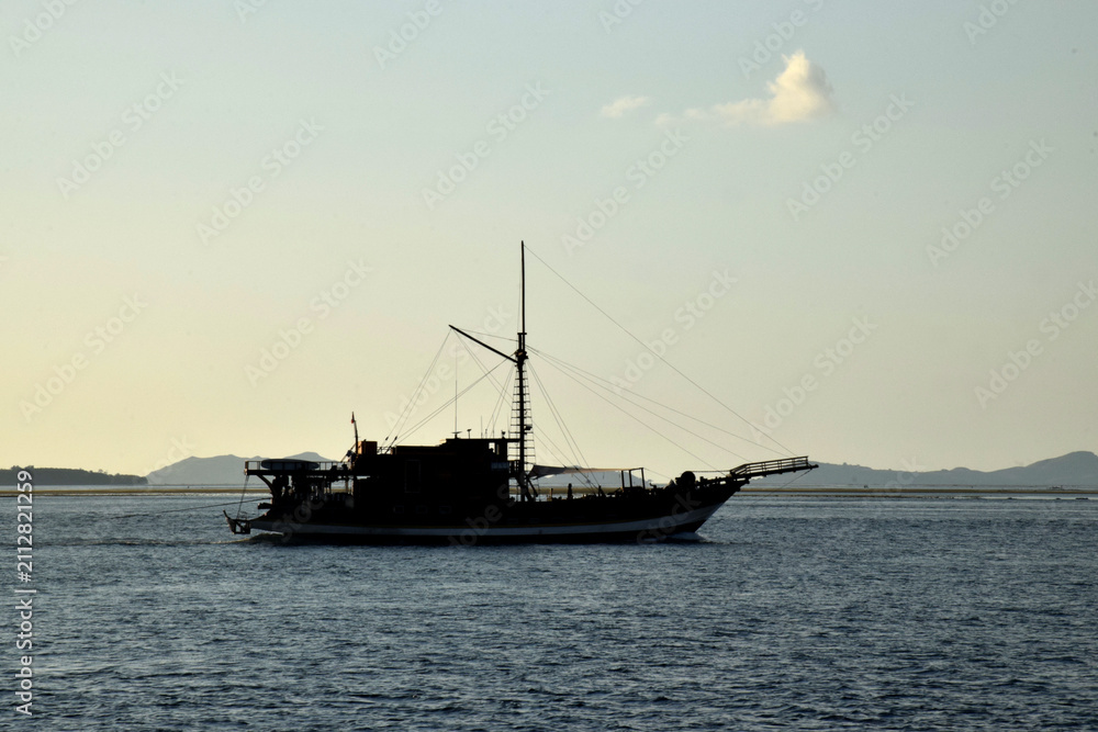 Fototapeta premium A Phinisi boat sails through the waters around Rinca and Padar Islands in Labuan Bajo, Indonesia, amidst beautiful natural scenery.