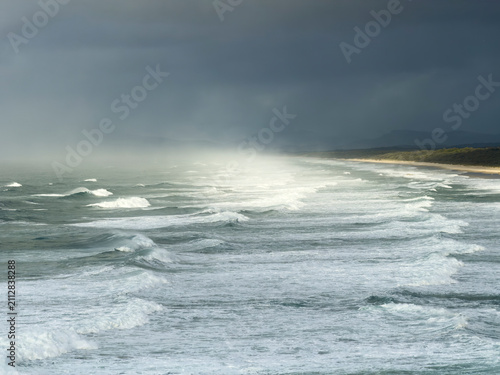 Powerful waves roll onto the coastline near Tacking Point Lighthouse in Port Macquarie, New South Wales, Australia, beneath dramatic morning storm clouds.