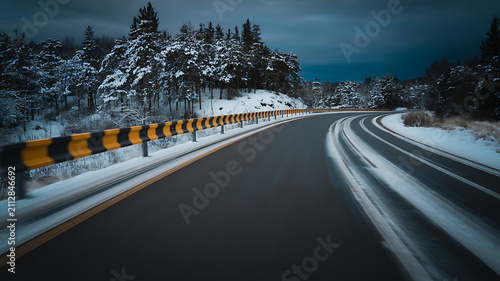 Winding winter road with snow covered trees and guardrail forest d