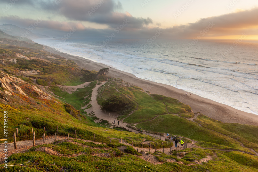 Fototapeta premium People hiking on a cliffside trail at Fort Funston in Daly City, California, enjoying a scenic walk down to the beach at sunset.