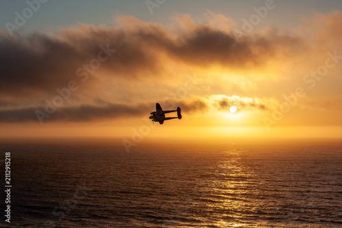 Bild auf Leinwand Silhouette of a model vintage Lockheed P-38 Lightning fighter plane flying over the Pacific Ocean at sunset in San Francisco, California, USA