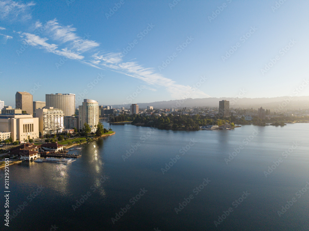 Fototapeta premium Urban skyline of Oakland California surrounding Lake Merritt, featuring downtown buildings, waterfront structures, and distant hills under a clear sky