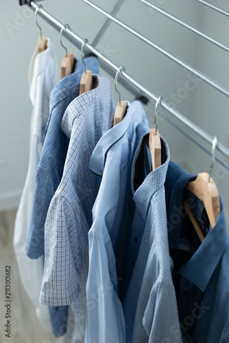 Foto A row of blue-toned casual shirts hanging on wooden hangers on a folding clothes drying rack