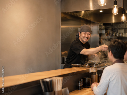 Cheerful Male Chef Serving Food to Customer in Busy Restaurant