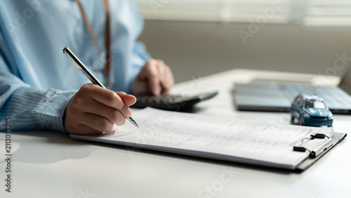 Foto Business woman completing a car insurance application with financial documents, calculator, and vehicle model, representing policy registration, underwriting, claims processing, and risk assessment