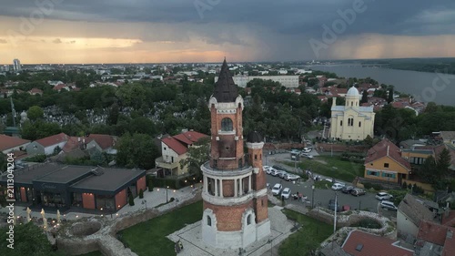 Cinematic aerial footage of Gardos Tower at dusk with dramatic cloudy sky and distant lightning over the Danube River, Zemun, Belgrade, Serbia.