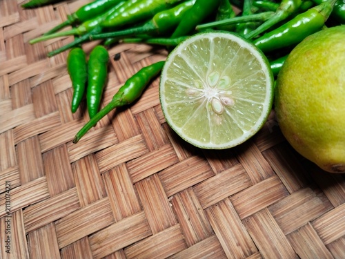Quadro su tela A lime is being cut in half on a bamboo tray, alongside green bird's-eye chilies