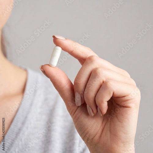 Woman holding a white medicinal capsule between her fingers close up