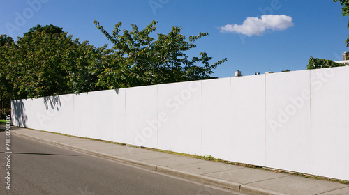 Blank white wall mockup on urban sidewalk with green trees