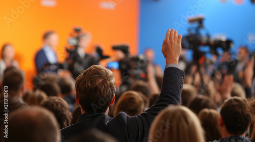 A man raises his hand during a political forum with cameras and speakers. Conceptualizing democracy, freedom of speech, and civic engagement.