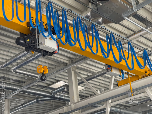 Yellow overhead crane beam with electric hoist hook in industrial factory. Bridge crane machinery background for manufacturing warehouse and engineering company website design