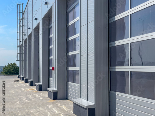 Industrial sectional overhead glass door with integrated wicket door for warehouse facility website design. Modern hangar panoramic door background for commercial architecture mockups.