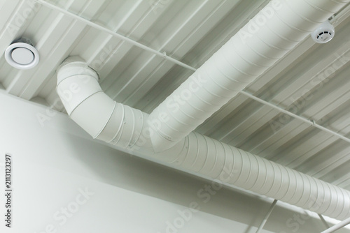 White spiral ventilation duct t-junction on ceiling for industrial hvac system website design. Air conditioning pipe background for climate control and engineering company mockups.