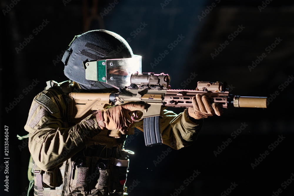 Obraz premium Tactical Soldier Aiming Assault Rifle While Wearing Helmet Visor And Body Armor In Low Light
