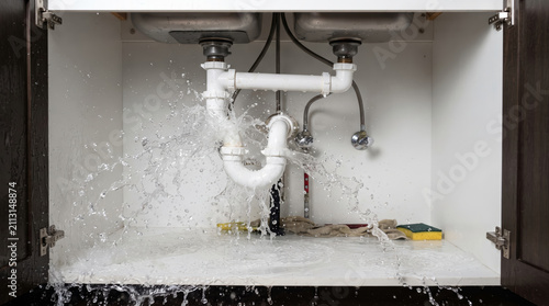 Burst pipe spraying water under kitchen sink cabinet creating emergency home plumbing leak damage