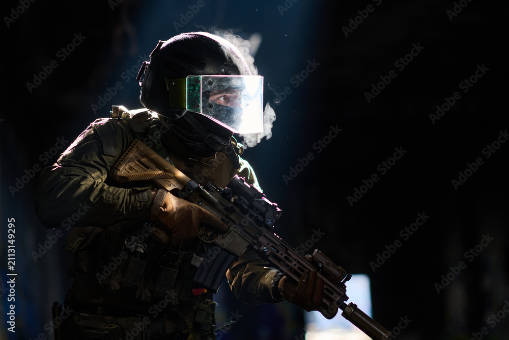 Obraz premium Tactical Soldier in Ballistic Helmet and Face Shield Holding Assault Rifle in Low Light Smoke