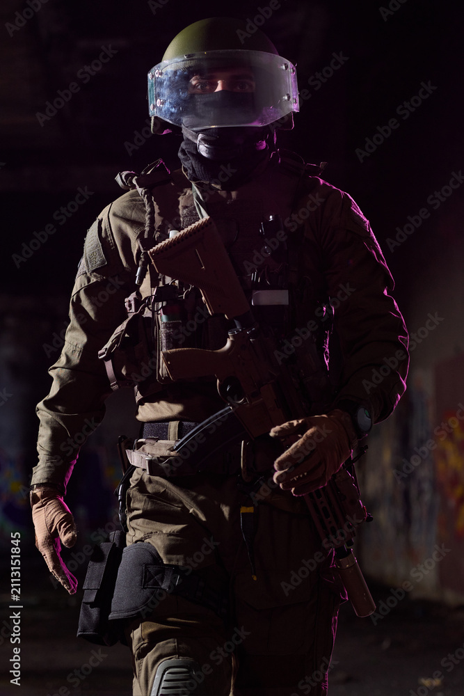 Obraz premium Armed Tactical Soldier In Protective Helmet And Visor Walking Through Dim Urban Environment