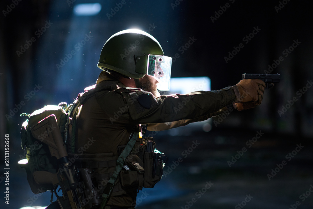Obraz premium Tactical Soldier Aiming Handgun in Dark Urban Environment Wearing Helmet and Protective Gear