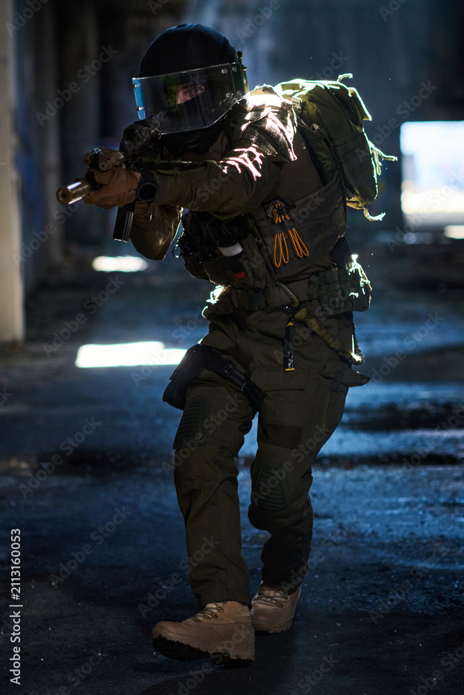 Fototapeta premium Tactical Soldier In Urban Combat Gear Aiming Assault Rifle Inside Dark Abandoned Building