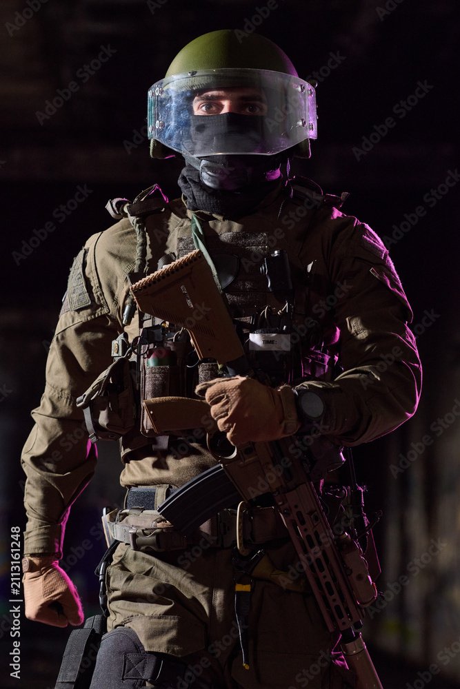 Obraz premium Armed Tactical Soldier in Riot Helmet and Body Armor Holding Assault Rifle in Low Light