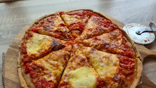 Freshly baked pizza cut into slices on a wooden board